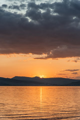 Obraz premium Burning red sunset on the river. Men riding boat. Silhouette of mountains on the background. Beautiful clouds in the sky.