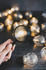 hand holding magnifying glass analyzing different ideas in shape of lightbulb string lights