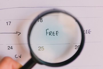 hand holding magnifying glass over a day marked as free on the calendar