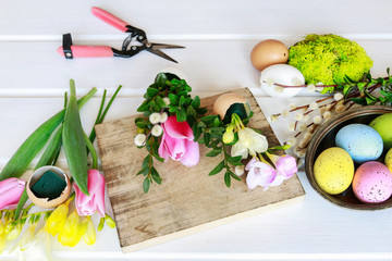 woman shows how to make Easter floral decoration with colorful eggs, tulips, freesias and buxus