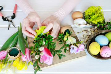 woman shows how to make Easter floral decoration with colorful eggs, tulips, freesias and buxus