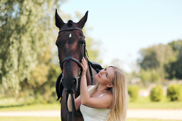 Fototapeta premium Young attractive blond woman hugs a brown horse.