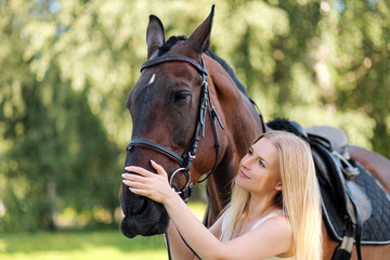 Fototapeta premium Young attractive blond woman hugs a brown horse.