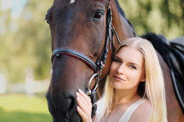 Young attractive blond woman hugs a brown horse.