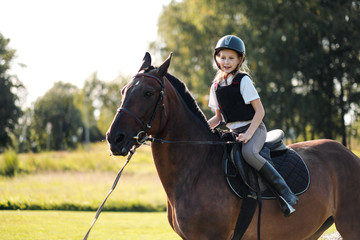 Girl teenager jockey sits on a brown horse in nature.