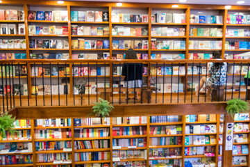 Blurred abstract background of bookshelves in book store, with a girl reading book in the store.
