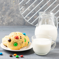 A cup of milk and homemade cookies decorated with colorful jelly beans candies on a gray table background. Copy space.
