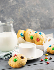 A cup of milk and homemade cookies decorated with colorful jelly beans candies on a gray table background. Copy space.