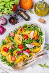 Vegetable fresh vegetarian salad of colorful tomatoes (cherry, yellow and orange), red onions, lettuce and Basil with spices and olive oil in a white plate. Selective focus