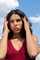 Close up portrait of a brunette woman rubbing her temples to alleviate an awful headache. Outdoors