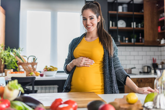 Young pregnant woman preparing healthy food with lots of vegetables at home kitchen