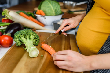 Young pregnant woman preparing healthy food with lots of vegetables at home kitchen
