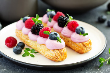 Homemade eclair with berry cream and fruits. . Pastry.