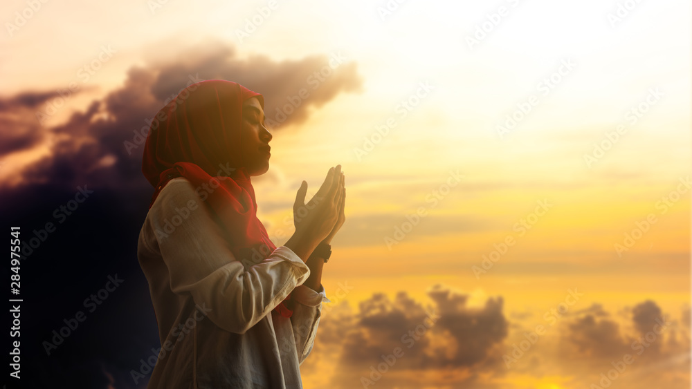 Poster silhoueitte of young muslim woman pray with beautiful sunset/ sunrise in background