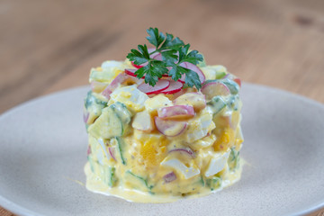 Delicious salad with cucumber, radish and egg with cream sauce in a plate on wooden background. Healthy food, close up