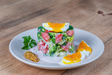 Delicious salad with broccoli, tomato, onion and boiled egg with cream sauce in plate on wooden background. Healthy food