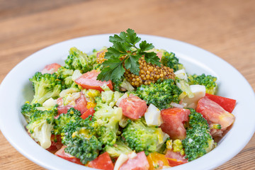 Delicious salad with broccoli, tomato, onion and boiled egg with cream sauce in plate on wooden background. Healthy food