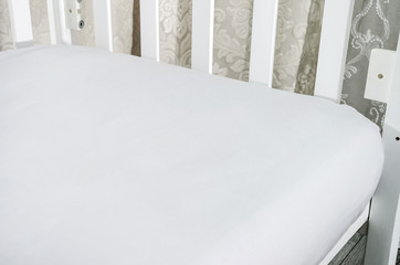 part of baby cot, close up. Mattress and sheets in white crib.