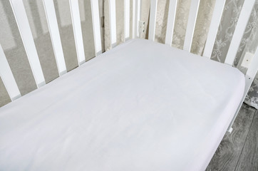 part of baby cot, close up. Mattress and sheets in white crib.