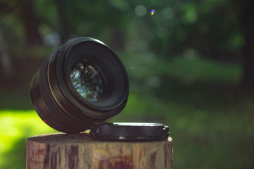 The lens for the camera is on a wooden stump on a blurred spring summer sunny green background....