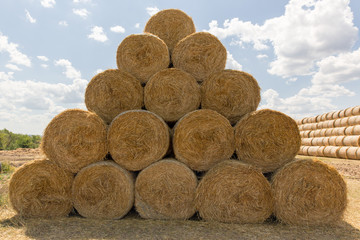 Bales of Golden straw are arranged in a field in the shape of a triangle against a blue sky with...