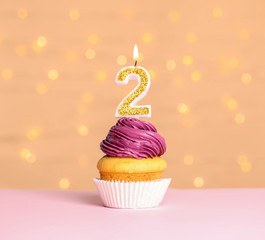 Birthday cupcake with number two candle on table against festive lights