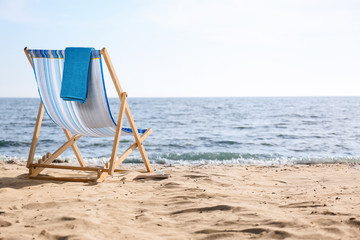 Lounger and towel on sand near sea, space for text. Beach objects