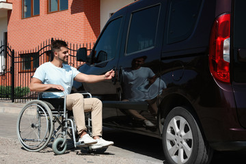 Young man in wheelchair opening door of his van outdoors