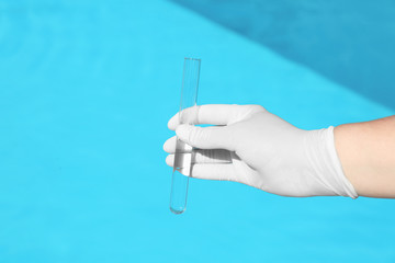 Woman holding glass tube with sample of swimming pool water to check PH level outdoors, closeup