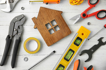 Set of repair tools and house figure on white wooden background, flat lay