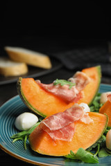 Fresh melon with prosciutto, mozzarella and arugula on table