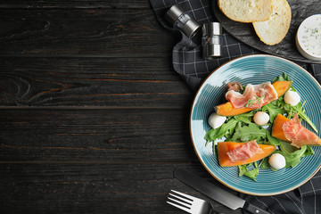 Flat lay composition of fresh melon with prosciutto on black wooden table. Space for text