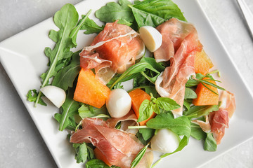 Fresh melon with prosciutto, mozzarella and arugula on light grey table, above view