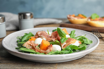 Fresh melon with prosciutto, mozzarella and arugula on wooden table