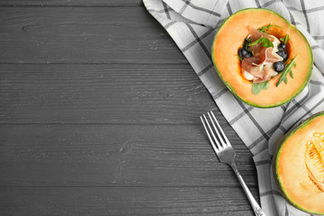 Flat lay composition of melon with prosciutto on grey wooden table. Space for text