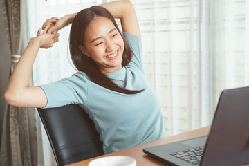 Asian girl sitting working with  laptop for long time. women is tired from working, stretching up, relaxed and smiling