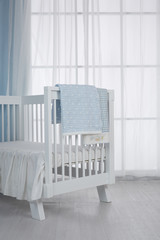 Children's bed in an empty room, lit by sunlight. There are white curtains, mats and jacquard quilts on the bed.