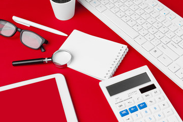 Red office desk table with blank notebook, keyboard and supplies. Top view with copy space. Flat lay.