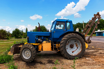 Soviet, blue tractor with blade and trencher stands on the side of the forest. Employment.