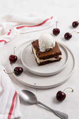 Homemade chocolate brownie with cream cheese, cherry and ice cream ball on the top on white background, homemade bakery and dessert. Bakery, confectionery concept. Side view, story, vertical