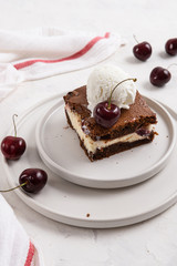 A piece of chocolate brownie with cream cheese, cherry and ice cream ball on the top on white background, homemade bakery and dessert. Bakery, confectionery concept. Copy space, side view