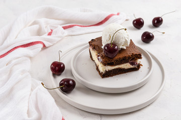 A piece of chocolate brownie with cream cheese, cherry and ice cream ball on the top on white background, homemade bakery and dessert. Bakery, confectionery concept. Copy space, side view