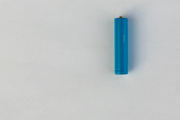 The battery or accumulator of dimension AA or AAA of blue color lies or costs on a sheet of white paper.