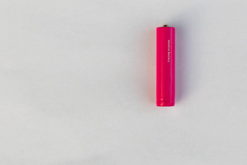 The battery or accumulator of dimension AA or AAA of pink color lies or costs on a sheet of white paper.