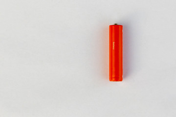 The battery or accumulator of dimension AA or AAA of orange color lies or costs on a sheet of white paper.
