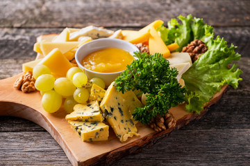 Cheese plate served with grapes, nuts and honey on a wooden background. Closeup