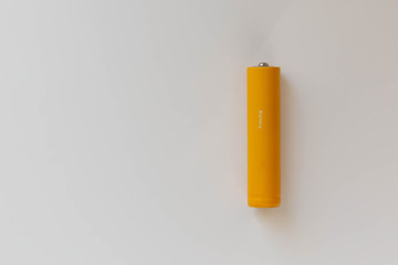 The battery or accumulator of dimension AA or AAA of yellow color lies or costs on a sheet of white paper.