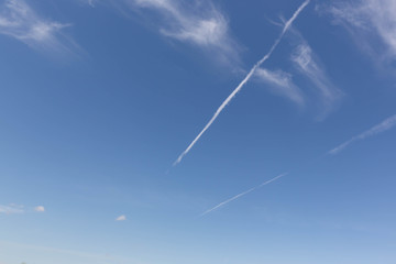 Naklejka na ściany i meble Two white jet tracks in a blue sky with sparse clouds.