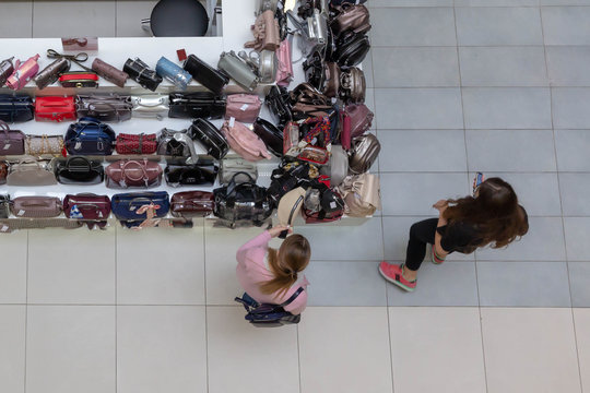Two young girls (women) stand at the counter with leather bags in the Mall and examine them.