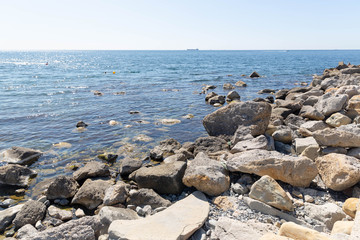 The rocky shore of the blue sea with the silhouette of a ship on the horizon.